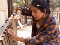 wooden-fence-repair-how-to-fix-8447789 A close-up of a carpenter replacing damaged slats on a wooden fence, tools and fresh lumber nearby.